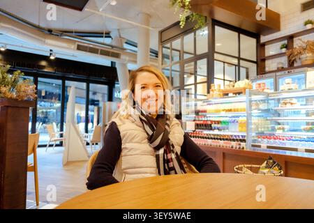 Junge blonde Frau, die an einem Tisch in einem hellen, modernen Café sitzt Stockfoto