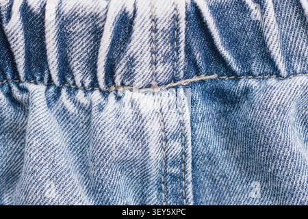 Horizontale Nahaufnahme aus blauem Denim-Jeans-Material mit elastischem Bund, Raffung und detaillierter Doppelnaht auf klassischer Baumwolle Stockfoto