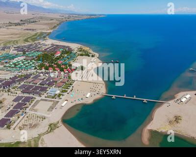 Ein riesiger Panoramablick auf ein Küstenresort am Rande des tiefblauen Issyk Kul Lake, der sich zum Horizont hin erstreckt Stockfoto