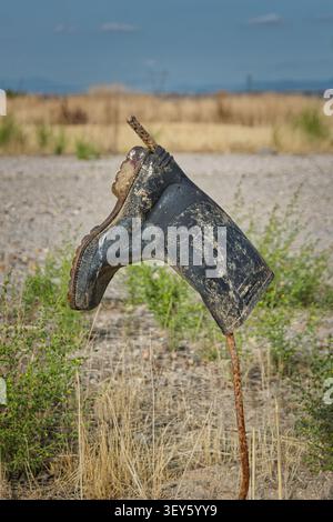Verlassene Gummistiefel hängen an einer rostigen Metallstange in einem trockenen, urbanen Ödland. Stockfoto