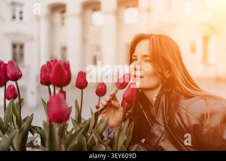 Frau Tulpen Sonnenuntergang junge Frau in Lederjacke riecht rote Tulpen in einem Stadtpark während der goldenen Stunde Stockfoto
