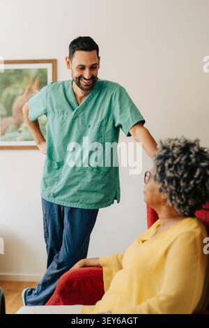 Lächelnde männliche Krankenschwester, die mit einer älteren Frau im Sessel im Pflegeheim spricht Stockfoto