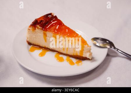 Käsekuchenscheibe mit Fruchtmarmelade auf weißem Teller mit Löffel. Stockfoto