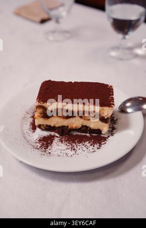 Tiramisu-Scheibe mit Kakaopulver auf weißer Platte mit Löffel. Stockfoto