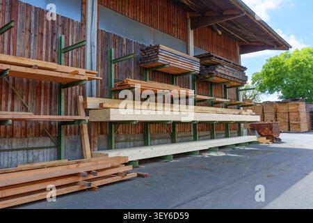 Holzdielen und -Balken werden auf grünen Metallregalen vor einem Holzgebäude in Otzberg-Lengfeld, Deutschland, gelagert. Stockfoto