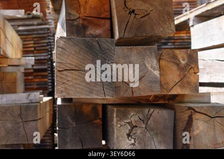 Nahaufnahme von gestapelten quadratischen Holzbalken in einem deutschen Holzhof mit Endkorn, natürlichen Rissen und verwitterten Texturen. Stockfoto