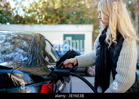 Die Hand der Frau, die das Kabel in das Elektroauto einsteckt, um die Batterie aufzuladen Stockfoto
