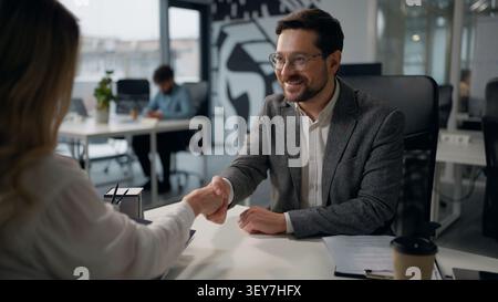 Zwei kaukasische Geschäftspartner im Büro Handshake Geschäftsmann, der Mappe mit Papieren Vertrag an Geschäftsfrau gibt Handshake Kooperationskredit Stockfoto