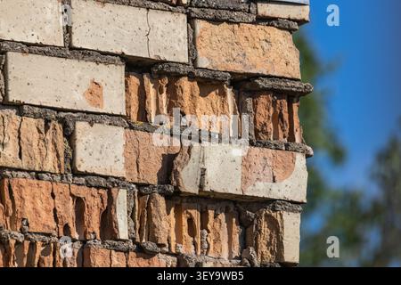 Detaillierte Ansicht einer alten sich verschlechternden Ziegelmauer mit gerissenem Mauerwerk, beschädigtem Mörtel und freiliegenden Hohlziegeln unter hellem Tageslicht im Freien. Stockfoto