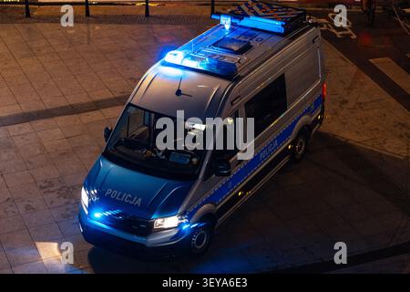 Aus der Vogelperspektive eines silbernen und blauen polnischen Polizeiwagens (Policja), der nachts auf einer Stadtstraße geparkt ist, mit blinkenden Notlichtern. Hochwinkelaufnahmen werden angezeigt Stockfoto