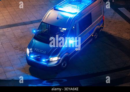 Hochwinkelaufnahme eines polnischen Polizeiwagens (Policja) bei Nacht mit blinkenden blauen Notlichtern auf einer asphaltierten Stadtstraße. Moderne Polizeipatrouillenfahrzeuge Stockfoto