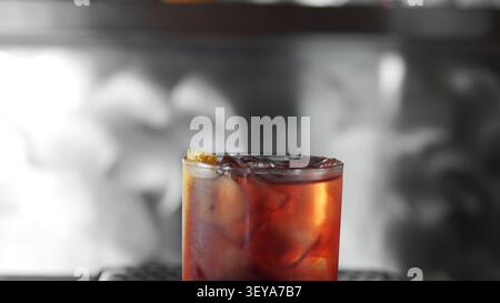 Negroni-Cocktail mit Eiswürfeln und Orangenschalen, reflektierendes Licht in einer dunklen Bar Stockfoto