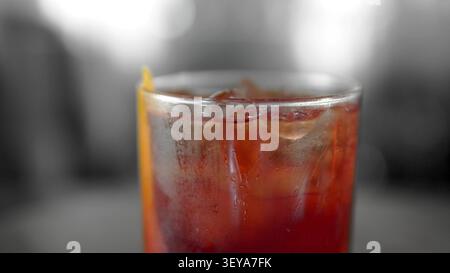 Kaltroter Cocktail mit Eiswürfeln und orangener Garnitur, Kondenswasser bildet sich auf dem Glas und zeigt ein erfrischendes Getränk Stockfoto