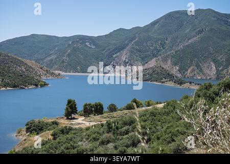 Aus der Vogelperspektive auf einen tiefblauen See, umgeben von sanften grünen Hügeln und zerklüfteten Bergkämmen. Stockfoto