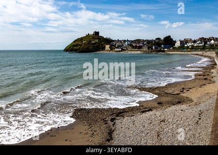 Weite Küstenansicht von Criccieth Beach mit Blick auf die Uferpromenade der Stadt und die weit entfernten Landzungen unter hellem Himmel, Gwynedd, Wales Stockfoto