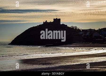 Silhouette des Sonnenuntergangs von Criccieth Castle auf seiner Landzunge mit Blick auf den Strand und das Meer in der Abenddämmerung, Gwynedd, Wales Stockfoto