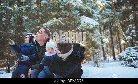 Glückliche Familie mit zwei Kindern, die einen Wintertag in einem verschneiten Wald genießen, während das ältere Kind auf etwas in der Ferne zeigt Stockfoto