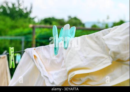 Helle Kleidung hängt an einer Wäscheleine mit Plastiktüchern, die draußen trocknen. Stockfoto