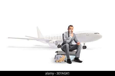 Besorgter Geschäftsmann, der auf einem Koffer sitzt und auf einen verspäteten Flug wartet, isoliert auf weißem Hintergrund Stockfoto