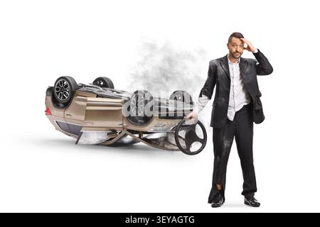 Schockierter Fahrer, der ein Lenkrad neben einem umgekippten Auto hält, isoliert auf weißem Hintergrund Stockfoto