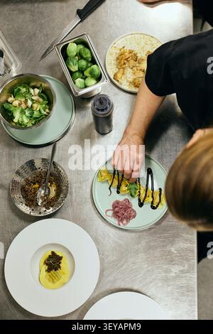 Direkt über dem Blick auf weibliche Köchin, die Pasta auf der Küchenzeile des Restaurants garniert Stockfoto