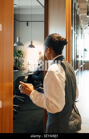 Geschäftsfrau hält Kaffee beim Betreten des Konferenzraums Stockfoto
