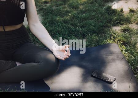 Frau sitzt in Meditationshaltung auf Matte draußen auf Gras. Digitaler Detox-Lifestyle, Trennung von Technologie, bewusste Reduzierung der Bildschirmzeit Stockfoto