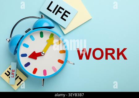 Work-Life-Balance. Wecker und Papiernotizen auf hellblauem Hintergrund, flach gelegt Stockfoto