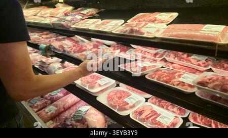 Einkäufer wählt verpacktes Frischfleisch aus der Kühltheke in einem Supermarkt Stockfoto
