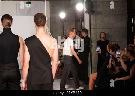 Berlin, Deutschland, 2. Juli 2026. Der polnische Modedesigner Mariusz Przybylski geht zum Runway-Finale seiner SS27 Kollektion Fashion Show auf der Fashionweek berlin. Gekleidet in einem klassischen weißen T-Shirt und einer dunklen Hose, geht der Designer an männlichen Models in asymmetrischen schwarzen Kleidungsstücken vorbei, um das Publikum zu begrüßen. In der ersten Reihe halten die Gäste Smartphones in der Hand, um den Moment unter der hellen Beleuchtung des Studios festzuhalten. Quelle: Felix Wolf/Alamy Live News Stockfoto