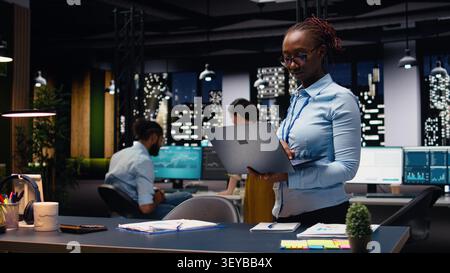 Porträt einer afroamerikanischen Frau im Büro, die Terminpläne auf einem Laptop verwaltet, Kalendertermine und Meetings organisiert. Fröhlicher junger Erwachsener, der Firmeninformationsdatensätze und -Daten zusammenstellt. Stockfoto