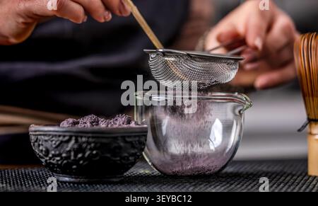 Frau, die Matcha-Tee zubereitete, indem sie Blue Matcha durch Ein Sieb siebt Stockfoto