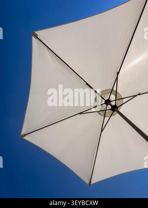 Niedrigwinkelaufnahme des weißen Sonnenschirms vor klarem blauem Himmel mit Kopierraum Stockfoto