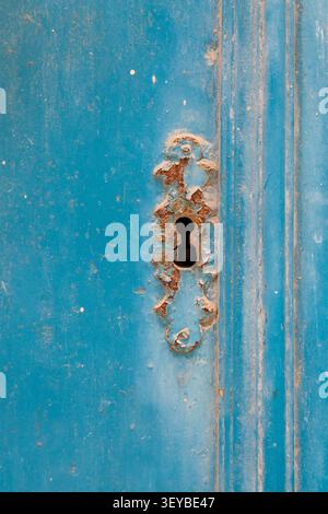 Ein rostig verziertes Schlüssellochrosett an einer verwitterten blau lackierten Holztür, mit abblätternder Farbe und altertümlicher Patina, in Gozo Stockfoto