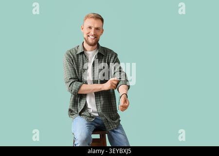 Lächelnder junger Mann, der die Ärmel hochkrempelt und auf dem Hocker sitzt Stockfoto