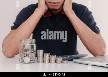 Ein Mann mit Taschenrechner, Laptop und Münzstapel auf dem Tisch. Verlust, Armut und Inflationskonzept. Stockfoto