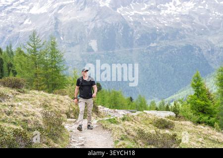 Ein Mann wandert auf einem felsigen Bergpfad, umgeben von üppigen Nadelbäumen, und fängt das Wesen einer abenteuerlichen Outdoor-Freizeitaktivität ein. T Stockfoto