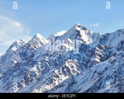 Fernaufnahme einer Gruppe von schroffen, stark Schnee- und eisbedeckten Berggipfeln, die den Rahmen unter klarem blauem Himmel dominieren Stockfoto