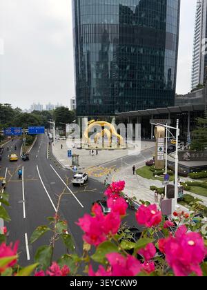 Goldene fünf Rams Skulptur Wahrzeichen in der Nähe des Guangzhou IFC Turms, eingerahmt von rosa Bougainvillea Blumen. Urbane Szene im Bezirk Tianhe, Guangzhou, China. Stockfoto