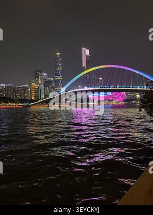 Guangzhou Haixin Sha Brücke beleuchtet mit Regenbogenlampen, die nachts auf Pearl River reflektieren, China City Skyline im Hintergrund. Stockfoto