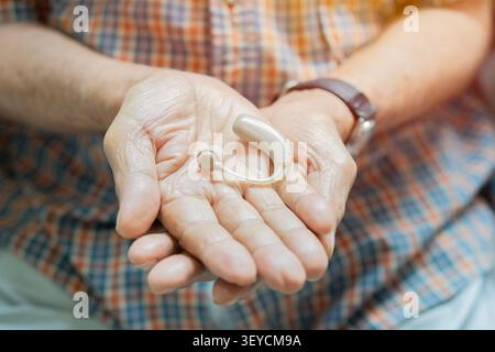 Nahaufnahme-Seniorenmann mit kariertem Hemd, der ein elektronisches Hörgerät in der Hand hält. Fokus auf das Gerät. Hörgerät, Hörlösungen Konz Stockfoto
