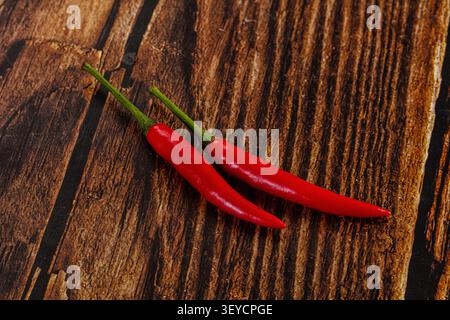 Leuchtend rote Chilischoten mit grünen Stielen ruhen schräg auf verwittertem dunklem Holz. Warmes Licht hebt die glänzende Textur mit kräftigem Farbkontrast hervor Stockfoto