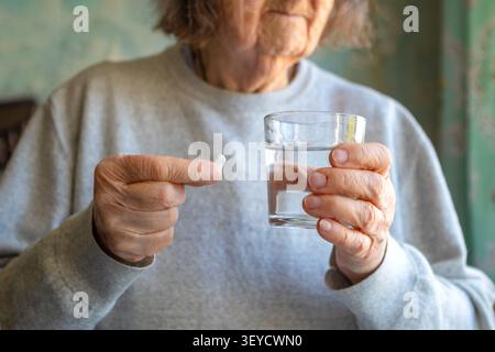 Ältere Frau, die zu Hause Medikamente mit einer Pille und einem Glas Wasser einnimmt Stockfoto