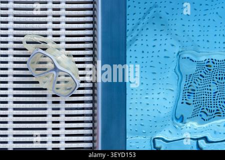 Schwimmbrille auf einer Bank am Pool mit entspannter Aussicht von oben in Blau und weiß Stockfoto