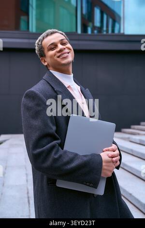 Ein hübscher Schüler in modischer Kleidung lächelt in einem urbanen Ambiente. Stockfoto