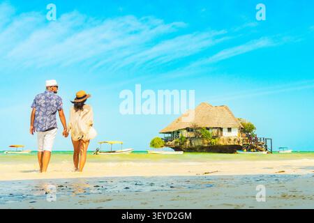 Ein junges Touristenpaar geht Hand in Hand zum berühmten Rock Restaurant an einem unberührten Südstrand Sansibars. Fängt authentische Romantik und Sommer-Ho ein Stockfoto