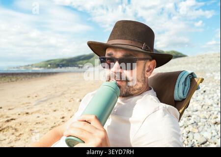 Mann trinkt aus einer wiederverwendbaren Flasche, während er sich draußen entspannt Stockfoto