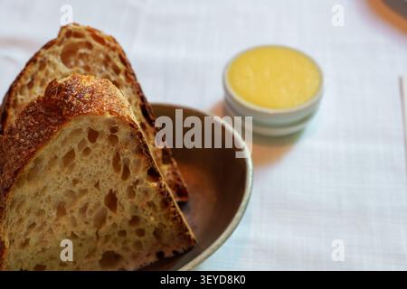 Nahaufnahme luftiger Sauerteigbrotscheiben in einer rustikalen Schüssel mit goldener Butter, die an ein warmes, einladendes Gourmet-Frühstück erinnert. Stockfoto