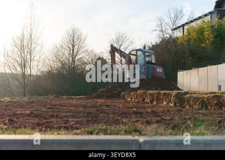 Der Bagger, der mit einem Löffel ausgestattet ist, wird Lehmboden mit Steinen vermischt. Die schweren Maschinen arbeiten fleißig auf der Baustelle Stockfoto