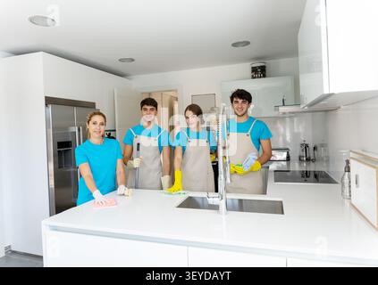 Gruppe professioneller Reinigungspersonal lächelt, während sie Hausreinigungsaufgaben in einer hellen Küche erledigt Stockfoto